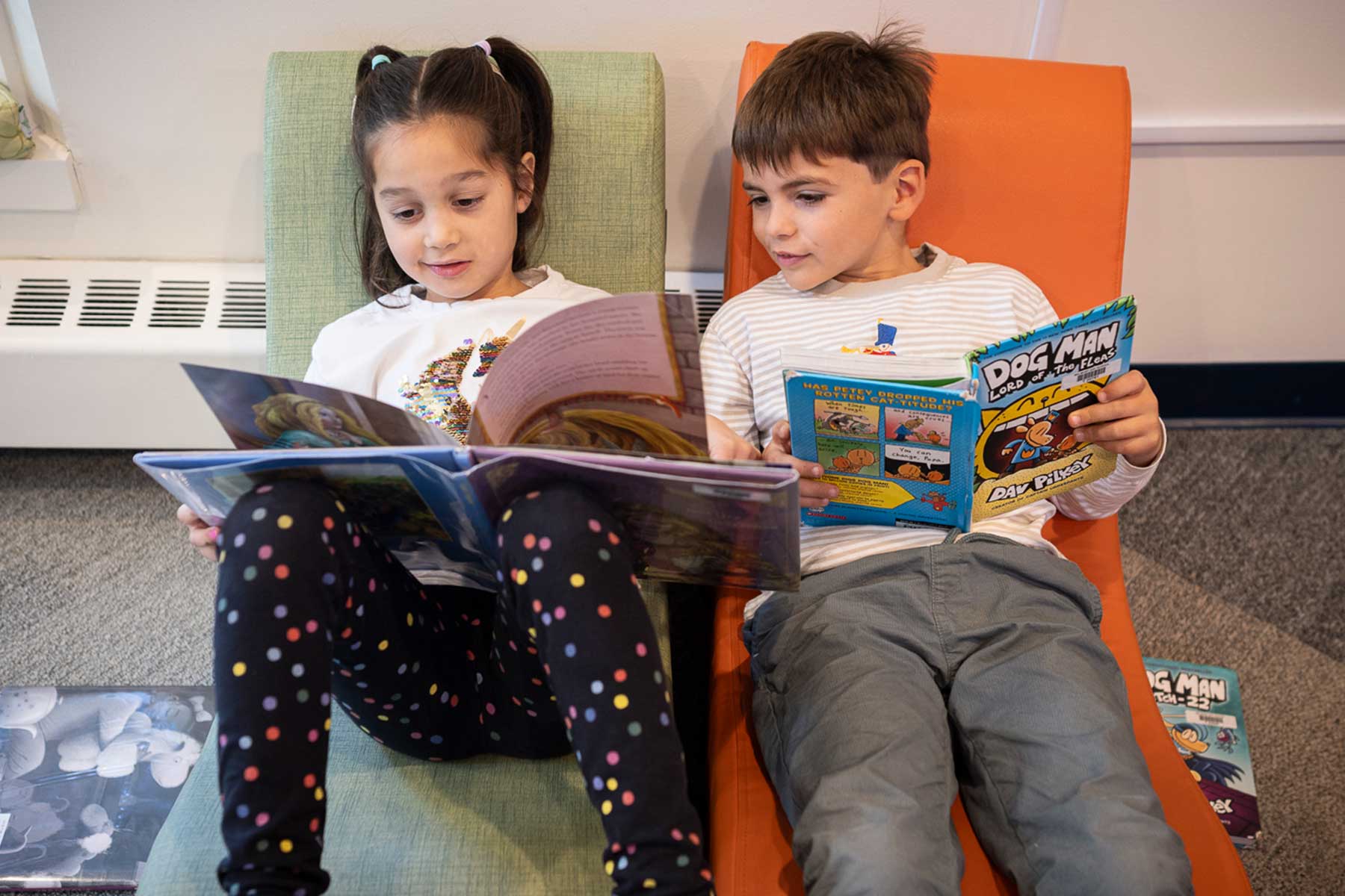 Two students relax in comfortable library chairs with picture books