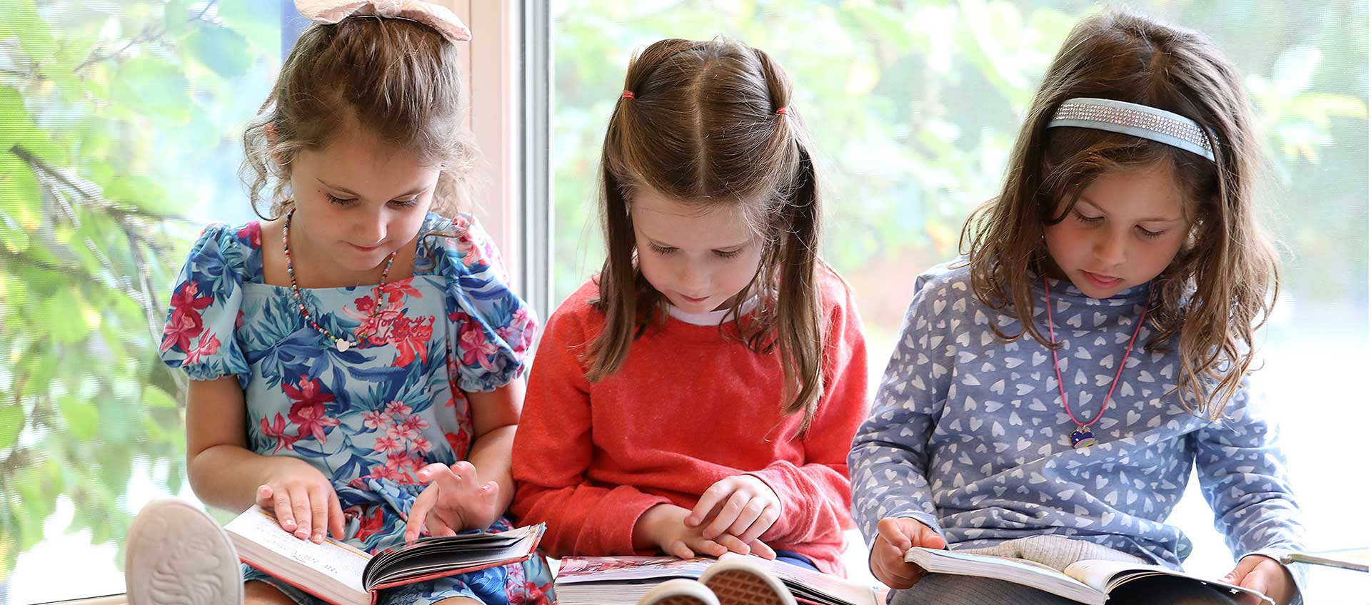 Three children sit in reading corner with books in the Erskine Library