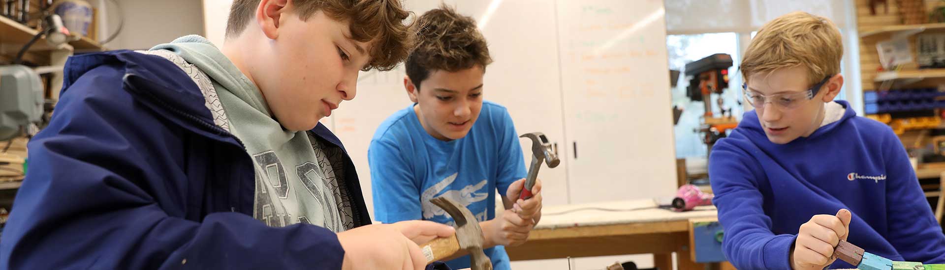 Three students in the woodworking studio, two are holding hammers and working on proects